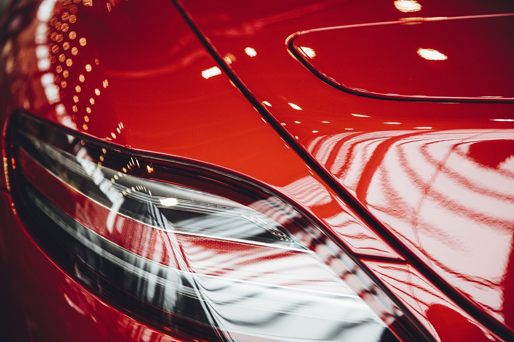 Close-up of a red sports car’s rear light and body, reflecting indoor lights and glass ceiling patterns after expert paint correction in New Orleans.