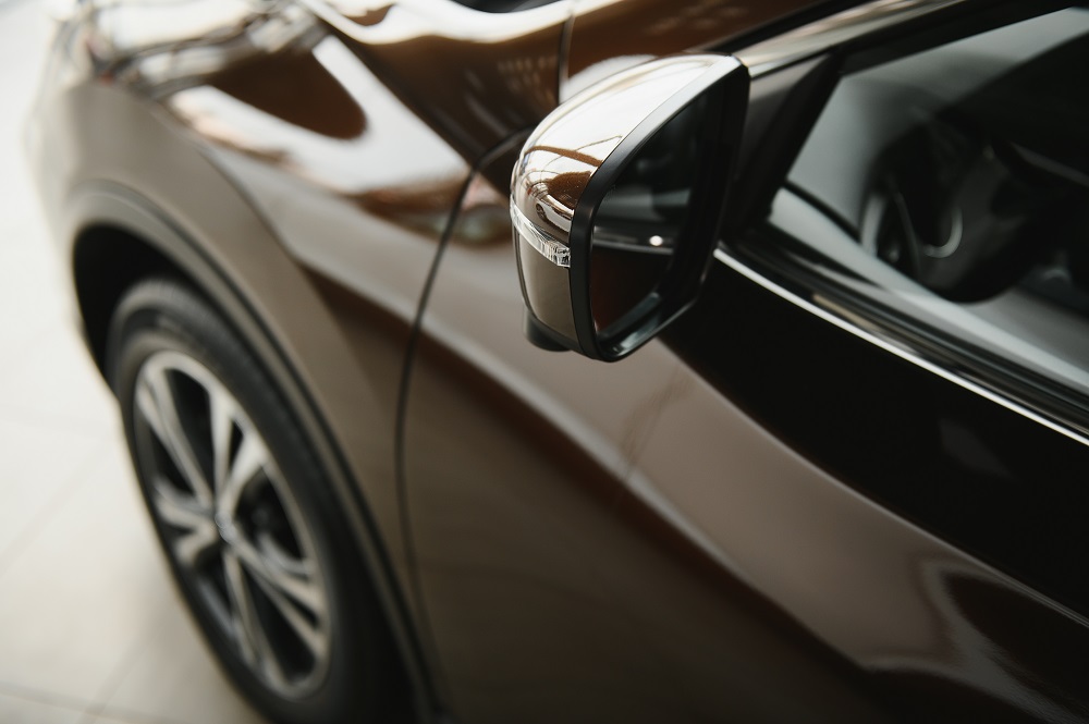 Close-up view of a car's side mirror and front wheel, with reflections gleaming on the shiny brown exterior—showcasing the quality of Car Detailing New Orleans.