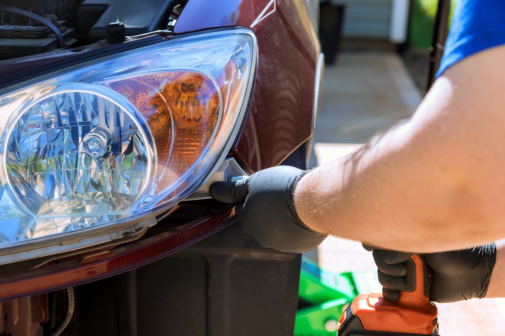 Wearing black gloves, a person uses a power tool to polish the headlight of a maroon car—showcasing expert Headlight Restoration New Orleans services.