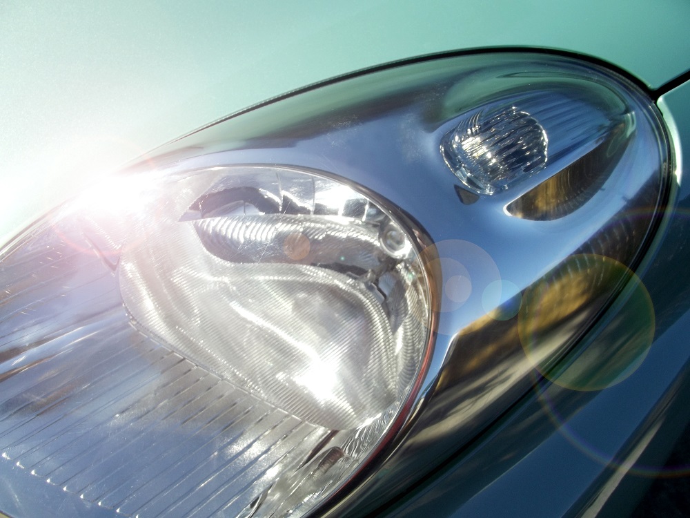 Close-up of a car’s headlight after Headlight Restoration New Orleans, with sunlight reflecting off the shiny surface and creating lens flares in the image.