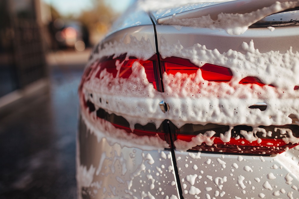 Close-up of the rear light of a silver car covered in soap suds during a professional Car Detailing New Orleans service.